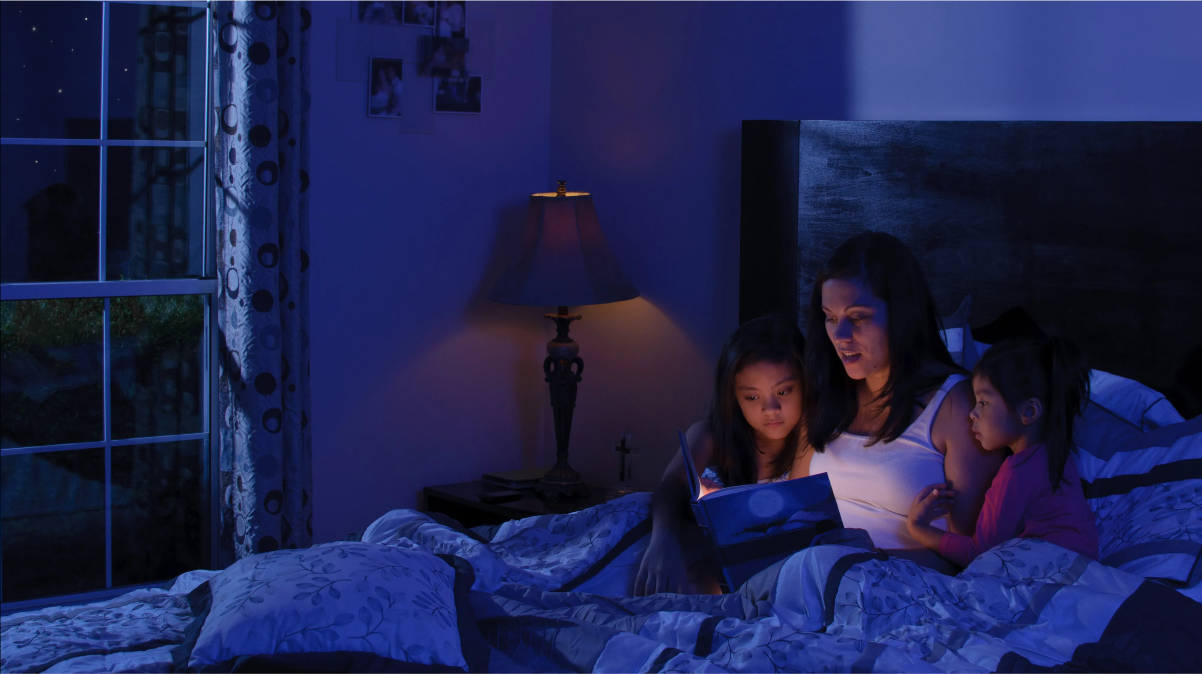 A mother reading a bedtime story to her daughters under cozy lighting, enjoying a peaceful night on a comfortable bed from Mattress To Door Stores in Mississauga, London, Scarborough, Brampton.
