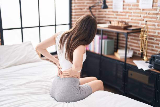 A woman sitting on a mattress designed for back pain relief, holding her lower back.