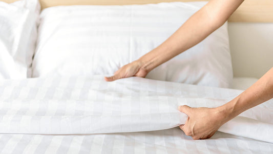 Hands smoothing a white checked bedsheet on a bed.